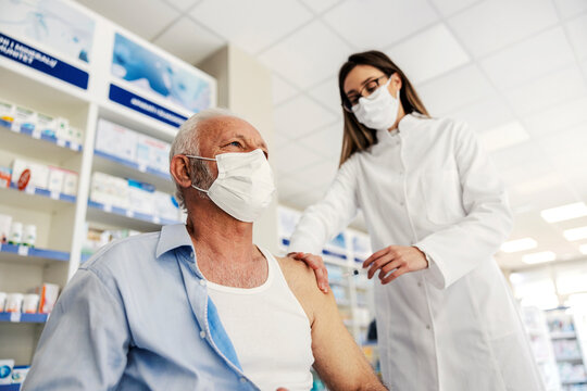 A nurse injecting corona virus vaccine into a senior's man shoulder at pharmacy.