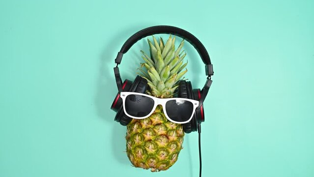 Creative pineapple with sunglasses and headphones dancing on blue background. Stop motion flat lay