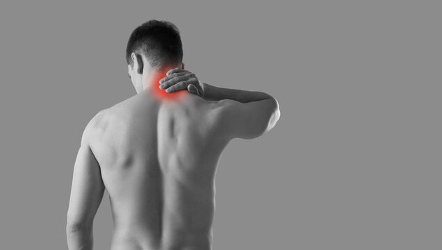 Neck pain. Rear view of man rubbing his sore neck while standing on gray banner background. Black and white image of naked unknown man holding on to sore spot that is highlighted in red. Copy space.
