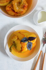 Stuffed peppers with rice and minced meat, in a white bowl, garnished with a sprig of basil on a concrete light background. Top view. Lunch
