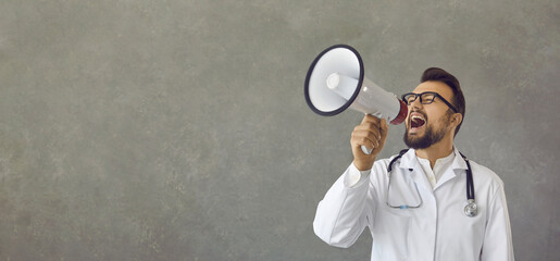 Young doctor in white lab coat with stethoscope speaking in bullhorn megaphone announcing important...