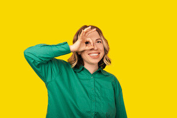 A photo of a cheerful young woman that i showing the ok sign holding it near her eye smiling at the camera