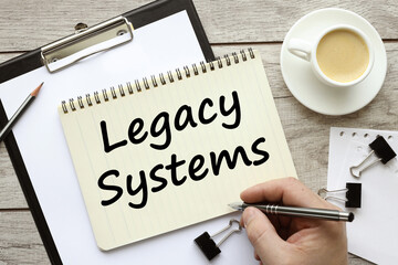Word writing text showing Legacy Systems. SOA application update business concept written on a notepad on a wooden background with a pen, a man's hand writes the text