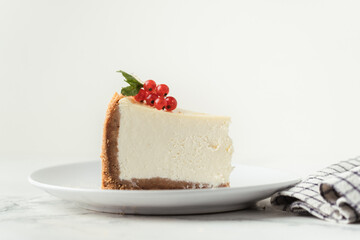 The piece of Classic New York cheesecake in the white plate decorated with red currant berries on the white background