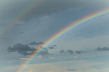 Huge rainbow in the sky with clouds. Sunny weather after rain. Multicolored rainbow as a result of light beams refraction in water droplets. Sign of peace