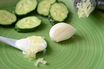 squeezed garlic and fresh cucumbers cut into slices on a green plate. white spoon of sour cream.
