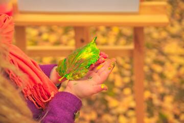 little girl holds in her hands a painted autumn leaf of a tree.