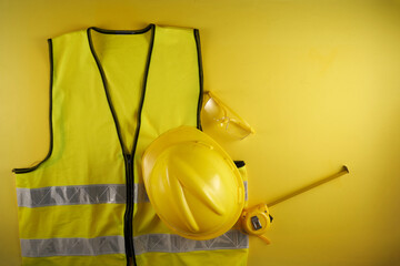 reflective vest ,tape measure  and hardhat against yellow background