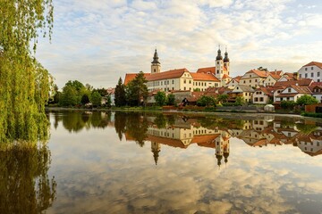 Fototapeta na wymiar Telc with historical buildings, church and a tower. Buildings in water reflection.