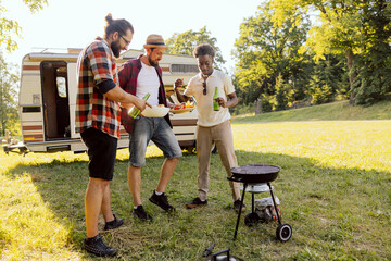 A group of friends spend time together in nature. Middle-aged men prepare a barbecue near an RV