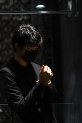 Portrait of an Asian man wearing a black suit and mask touching sleeves