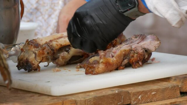 The cook cuts pieces of fresh fried meat from the bone with a knife. Butcher's hands in black rubber gloves