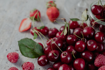 Appetizing, fresh, juicy, ripe cherry,  strawberry and raspberry assortment on light gray background.  Cherry leaf in the background. 