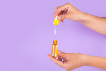 Serum bottle in female hands, top view. Yellow moisturizer for skin care. Nourishing essential oil...