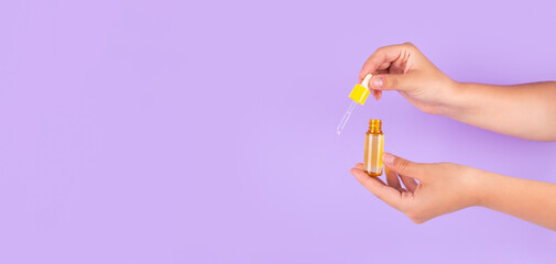 Beautiful groomed woman's hands with yellow serum with vitamin c on purple background. Nourishing...