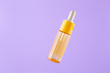 glass yellow bottle with pipette with essential oil on purple background top view. Aromatic cosmetic product for skin hair care Moisturizing beauty product with vitamin C close up