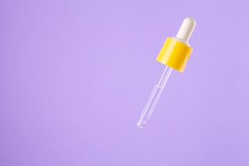 Essential clear oil or serum in pipette isolated on pastel purple background close up. cosmetic pipette