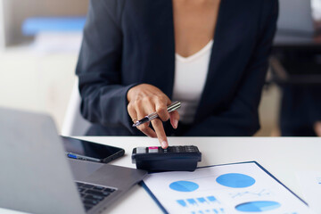 Close-up of businesswoman using calculator to calculate and record company marketing data.