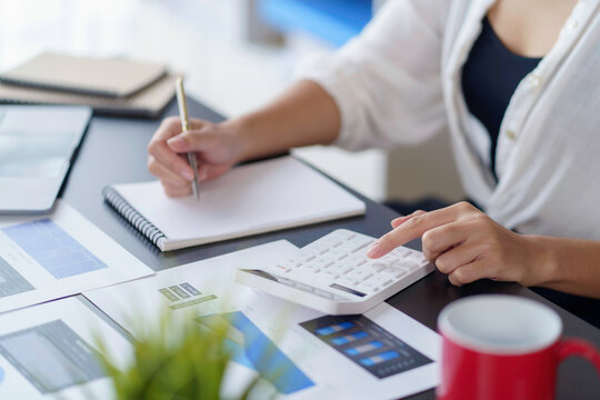 Close-up of businesswoman using calculator to calculate and record company marketing data.