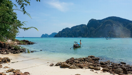 Long-tail boat on sea near the tropical beach with white sand and rocks and mountains in the background, Koh Phi Phi, Thailand