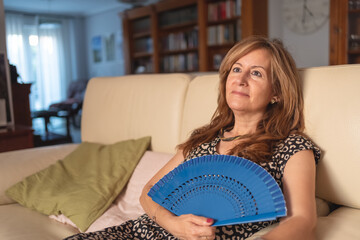Woman sitting on the sofa of her house and sweating from the high temperatures of summer.