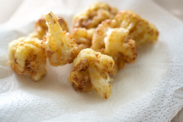 Golden deep fried cauliflower florets on a paper towel to drain, cooking creative with vegetable copy space, selected focus