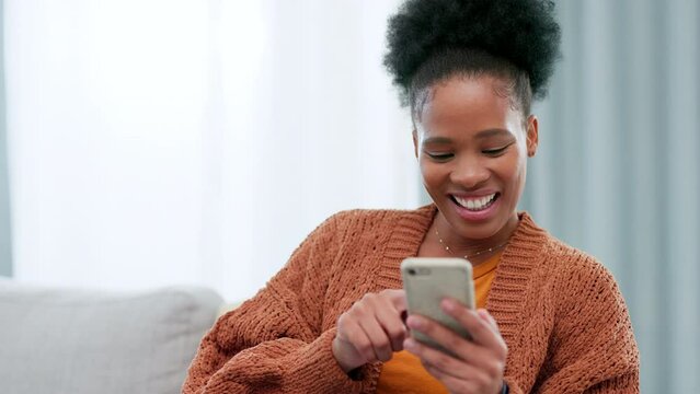 Happy woman scrolling and browsing through social media online with her phone while sitting on the couch at home alone. One cheerful black female typing and sending a text message to her friend