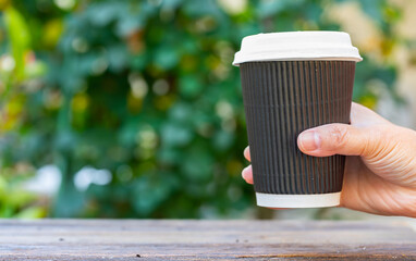 hand holding a paper coffee cup on blurred garden background.