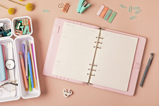 Home office desktop over pink background. Modern workspace with notebook, office stationary in plastic organizers