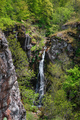 Scenic mountain waterfall in vivid green forest streaming down the mossy cliff - 518761899