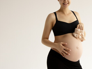 Woman standing and touching with hands her naked big belly. Isolated on gray background. Emotional...