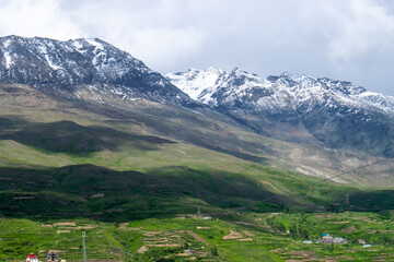 Fototapeta na wymiar Vast landscape of snow capped mountains and lush green terrace farming.Small village houses can also be seen and beautiful sun shadow passing through mountains.Monsoon view of himalayan village india.