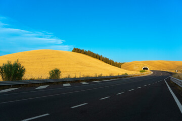 Strada che passa attraverso le colline toscane con campi di grano al tramonto