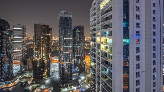 Tall residential buildings at JLT district aerial night timelapse, part of the Dubai multi commodities centre mixed-use district. Panoramic view to skyscrapers