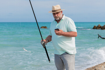 Focused mature man with a fishing rod and a phone
