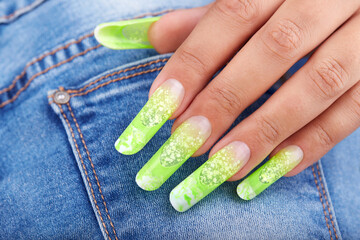 Hand with long artificial French manicured nails colored with green neon and white on jeans denim textile background