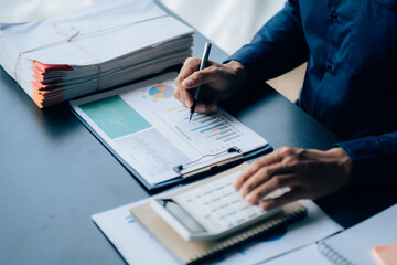 The hands of a male businessman are analyzing and calculating the annual income and expenses in a financial graph that shows results To summarize balances overall in office