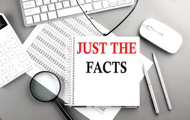 JUST THE FACTS text on notepad on chart with keyboard and calculator on grey background