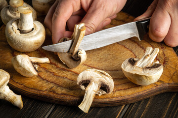 Experienced chef cuts mushrooms Agaricus with knife to prepare delicious food. Set of vegetables on a vintage kitchen table