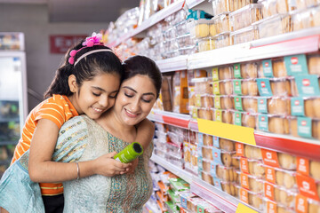 Happy mother and daughter reading product information while shopping at supermarket