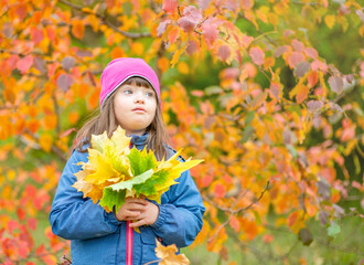 Smiling young girl with Downs syndrom holds bouquet of autumn leaves. Empty space for text