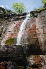 Scenic Cungulj waterfall cascading down the red, wet cliff covered by green moss - 518781812