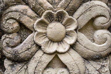 An aged flower relief carved out of a natural rock with black dirt residues.