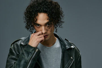 Obraz na płótnie Canvas Sexy pretty stylish tanned curly man leather jacket looks at camera posing isolated on over gray studio background. Cool fashion offer. Huge Seasonal Sale New Collection concept. Copy space for ad