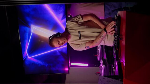 DJ working in club. Young adult person in headphones mixing music playlist indoors. Nightclub party concept. Slow motion vertical video