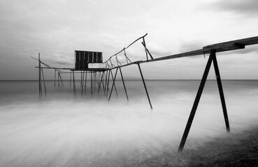 Fototapeta premium Black and white long exposure shot tulle effect near coastline with tiny wooden fisherman pier abstract photo 