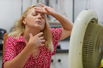 Woman cooling herself with fan. The girl escapes from the heat with a home fan at home. Exhausting...