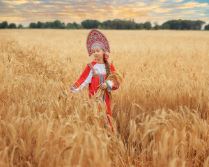 Littl girl kid in Russian national sarafan and a kokoshnik standing in a golden wheat field in summer day
