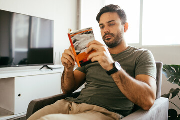 Young man reading book in the living room.