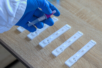 un médecin avec des gants bleus traitant plusieurs autotests covid 19 positifs et négatifs (sras cov 2) et avec un tube avec solution d'extraction dans la main - obrazy, fototapety, plakaty